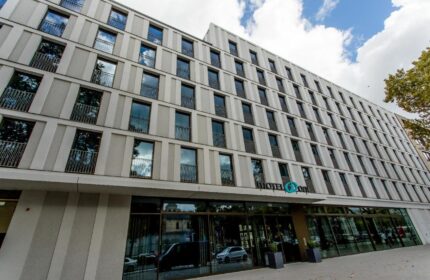 Motel One Köln-Neumarkt exterior. Gay-friendly hotel in Cologne, Germany. Modern building facade with many windows and the hotel's logo.