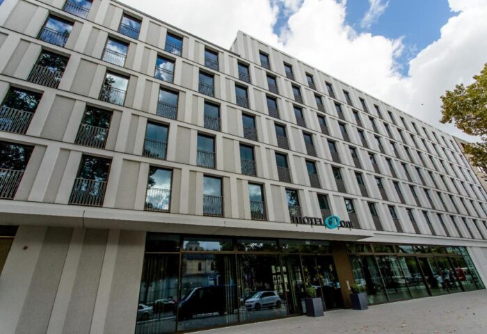 Motel One Köln-Neumarkt exterior. Gay-friendly hotel in Cologne, Germany. Modern building facade with many windows and the hotel's logo.
