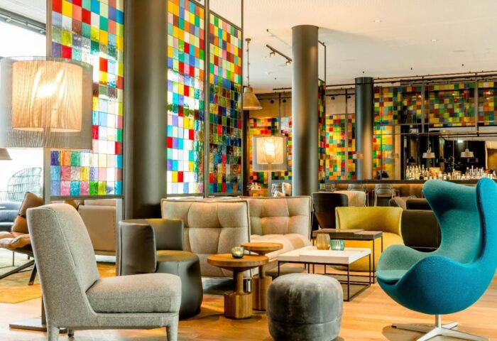Motel One Koln-Neumarkt lobby. Gay-friendly hotel with colorful glass panels, stylish seating, and a modern bar area. Perfect for gay travelers.