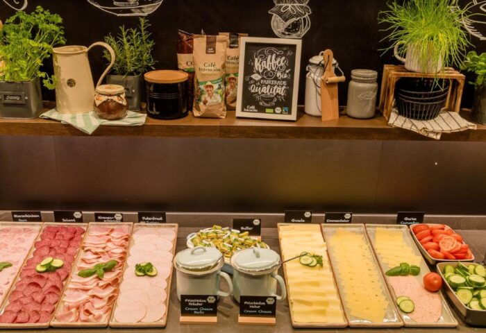Breakfast buffet at Motel One Koln-Neumarkt, a gay-friendly hotel. Selection of cold cuts, cheese, and fresh produce. Coffee and herbs.