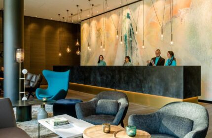 Motel One Koln-Neumarkt lobby. Gay-friendly hotel reception with staff, modern design, stylish seating area. Ideal stay in Cologne, Germany.