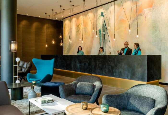 Motel One Koln-Neumarkt lobby. Gay-friendly hotel reception with staff, modern design, stylish seating area. Ideal stay in Cologne, Germany.