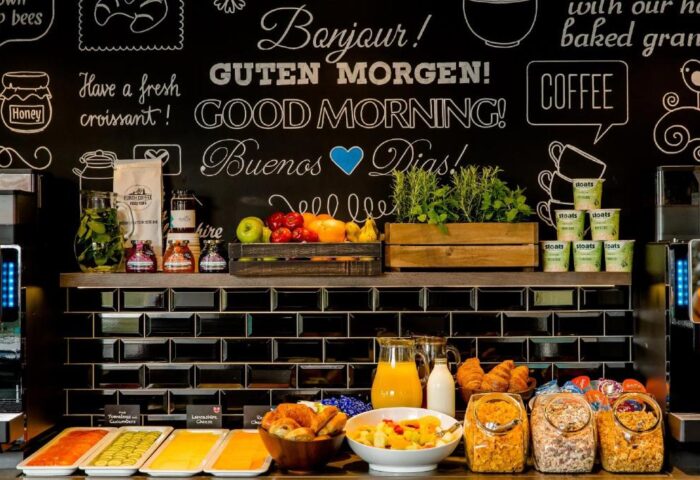 Breakfast buffet at Gay-Friendly Motel One London-Tower Hill. Fresh croissants, cereals, fruits, juices, and coffee. Bonjour! Guten Morgen! wall art.