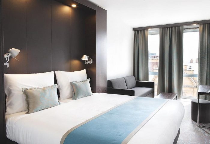 Motel One Manchester-Piccadilly room. Gay-friendly hotel bedroom with double bed, sofa, city view. Modern design, comfortable for gay travelers.