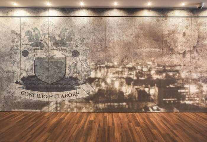 Motel One Manchester-Piccadilly wall detail. Coat of arms with Concilio et Labore on a banner. Gay-friendly hotel interior with wood floor.