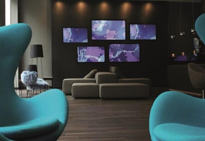 Motel One Manchester-Piccadilly interior. Lounge area with blue chairs, sofa, and wall-mounted screens. Gay-friendly hotel.