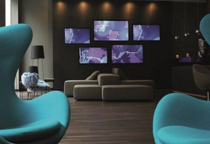 Motel One Manchester-Piccadilly interior. Lounge area with blue chairs, sofa, and wall-mounted screens. Gay-friendly hotel.