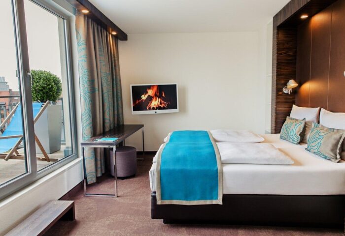 Motel One München Sendlinger Tor room. Gay-friendly hotel featuring a balcony with deck chairs, a double bed, and a TV. Modern design.