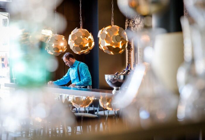 Motel One München Sendlinger Tor bar area. Bartender in blue shirt, suspenders. Modern lighting. Gay-friendly hotel in Munich, Germany.