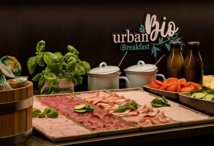 Motel One München Sendlinger Tor's breakfast buffet. Cold cuts, cheese, tomatoes, cucumbers, and fresh basil are displayed. Gay-friendly hotel.