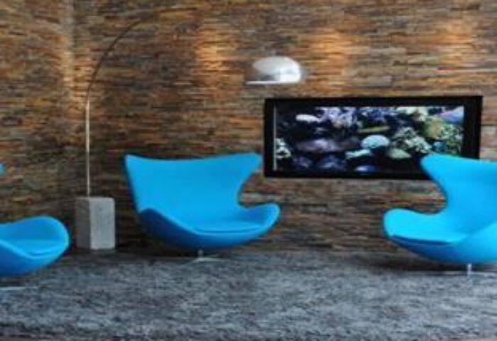 Lounge area at Gay-Friendly Motel One München Sendlinger Tor. Blue chairs, stone wall, aquarium TV. Modern design, welcoming atmosphere. Munich hotel.