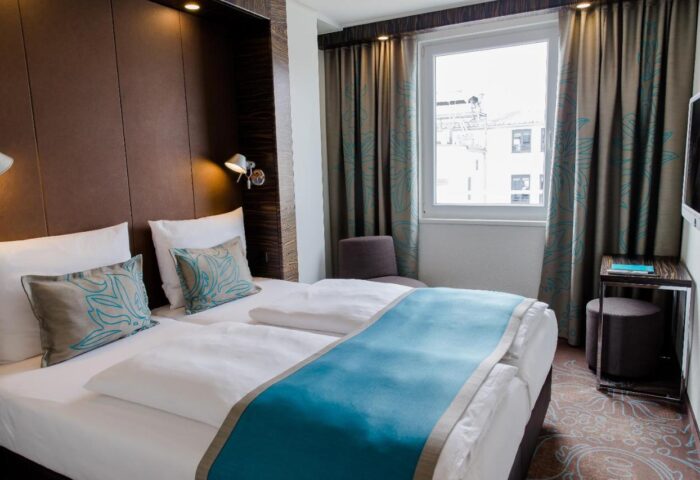 Motel One München Sendlinger Tor room. Gay-friendly hotel room with twin beds, blue accents, and modern design. Munich hotel for gay travelers.