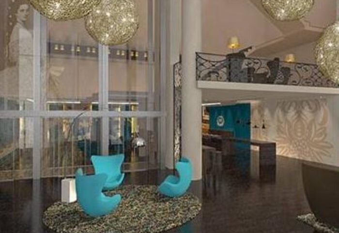 Motel One Wien Westbahnhof lobby. Gay-friendly hotel interior with modern design, turquoise chairs, and stylish lighting. Vienna hotel for gay travelers.