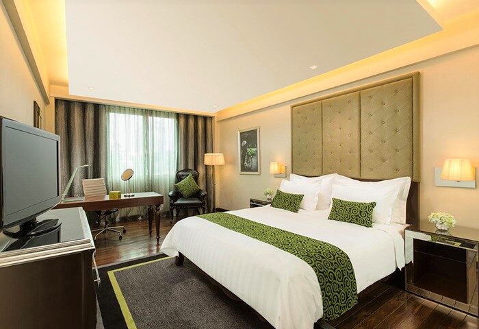 Movenpick Hotel Hanoi room. Gay-friendly hotel with a bed, desk, chair, and TV. Modern design with green accents. Comfortable stay in Hanoi.