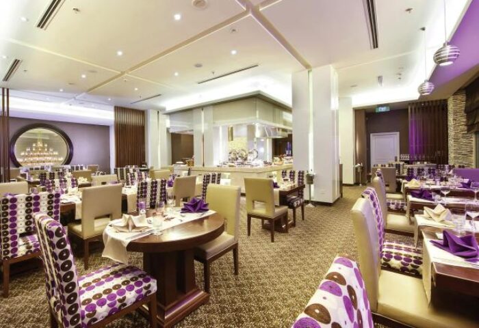 Movenpick Hotel Hanoi's restaurant. Elegant dining area with tables set, stylish chairs, and purple accents. Gay-friendly hotel Hanoi.
