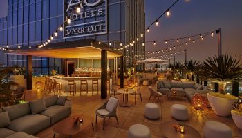 Rooftop bar at the gay-friendly Moxy Downtown Los Angeles hotel. String lights, seating areas, and a bar create a stylish, inviting space.
