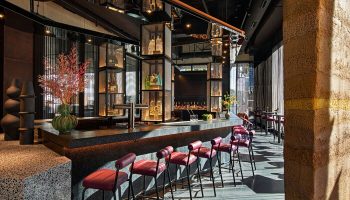 Bar at Moxy Downtown Los Angeles, a gay-friendly hotel. Stylish interior with bottles on display, seating, and modern design elements. Great for gay travel.