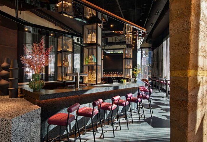 Bar at Moxy Downtown Los Angeles, a gay-friendly hotel. Stylish interior with bottles on display, seating, and modern design elements. Great for gay travel.