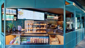 Moxy Downtown Los Angeles gay-friendly hotel cafe. Turquoise design with pastries, drinks, and snacks. Menu board above the display case.