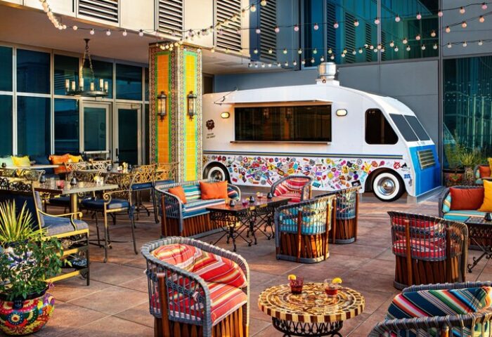 Moxy Downtown Los Angeles gay-friendly hotel outdoor patio with colorful furniture, string lights, and a food truck. Trendy, vibrant space.
