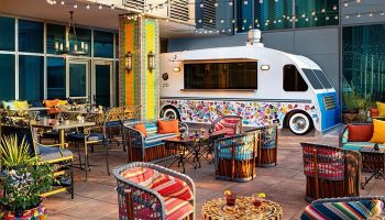 Moxy Downtown Los Angeles gay-friendly hotel outdoor patio with colorful furniture, string lights, and a food truck. Trendy, vibrant space.