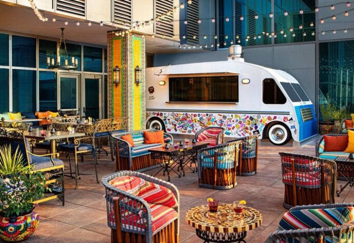 Moxy Downtown Los Angeles gay-friendly hotel outdoor patio with colorful furniture, string lights, and a food truck. Trendy, vibrant space.
