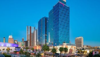 Moxy Downtown Los Angeles, a gay-friendly hotel. High-rise building with palm trees in the foreground. Great location for gay travelers.