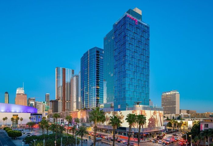 Moxy Downtown Los Angeles, a gay-friendly hotel. High-rise building with palm trees in the foreground. Great location for gay travelers.