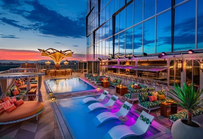 Rooftop pool at Moxy Downtown Los Angeles, a gay-friendly hotel. Lounge chairs, bar, and city views at dusk. Perfect for LGBTQ+ travelers.