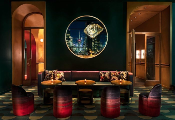 Moxy NYC Chelsea gay-friendly hotel lounge area. Stylish seating, round tables, and a circular window with a city view. Chic interior design.