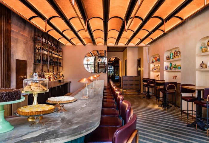 Interior of Moxy NYC Chelsea, a gay-friendly hotel. Bar with cakes, pastries, and drinks. Stylish design, seating, and ambiance.