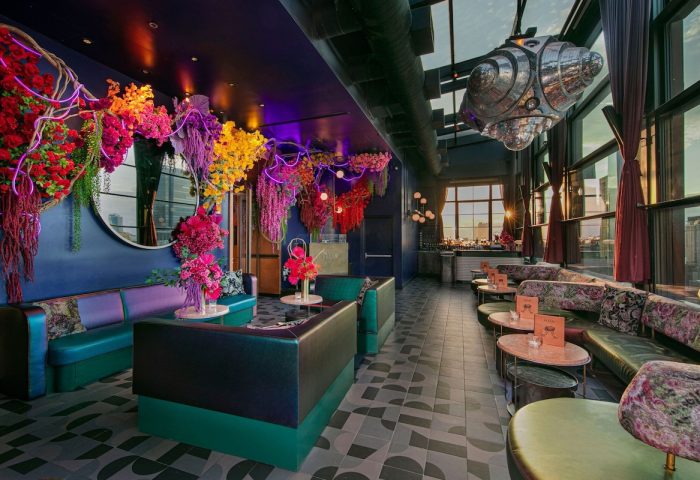 Moxy NYC Chelsea's vibrant, gay-friendly rooftop bar. Floral decor, colorful seating, and city views create an inviting atmosphere.
