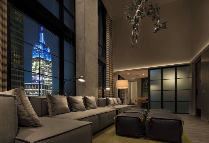 Moxy NYC Chelsea gay-friendly hotel room at night. Empire State Building view from window. Modern design, comfortable seating. NYC travel.