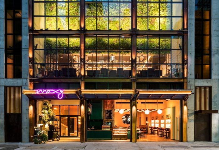 Moxy NYC Chelsea hotel exterior. Gay-friendly hotel with a neon sign, greenery, and a bar. A top choice for gay men visiting NYC.