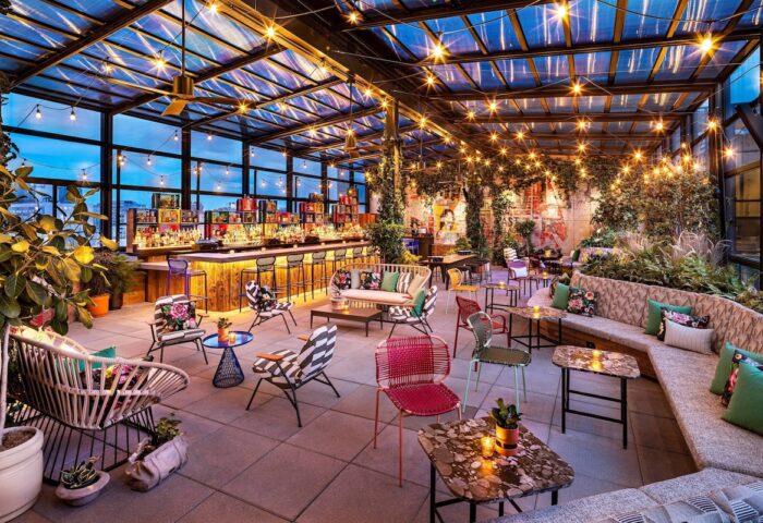Stylish rooftop bar at Moxy NYC East Village, a gay-friendly hotel. Cozy seating, lush greenery, and city views. Perfect for gay travel.