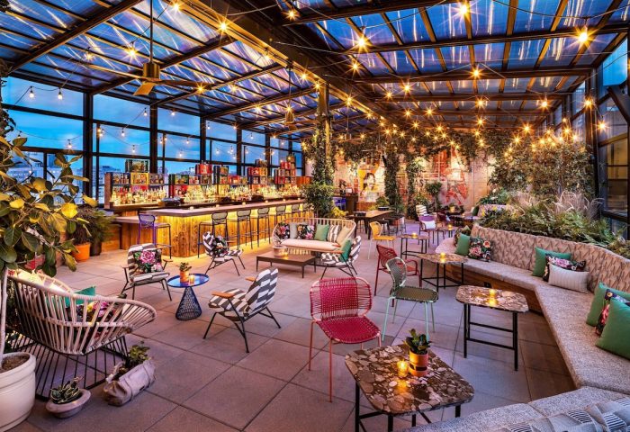 Stylish rooftop bar at Moxy NYC East Village, a gay-friendly hotel. Cozy seating, lush greenery, and city views. Perfect for gay travel.