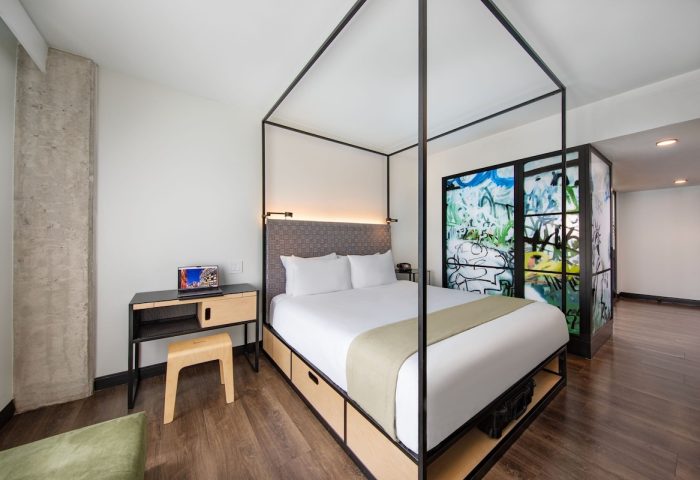 Moxy NYC East Village hotel room. Gay-friendly hotel with king bed, graffiti art, desk, and stool. Modern design for gay travelers.