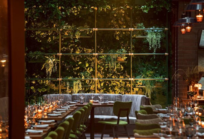 Moxy NYC East Village gay-friendly hotel restaurant. Tables set for dining, greenery wall, and warm lighting. Ideal for gay travelers.