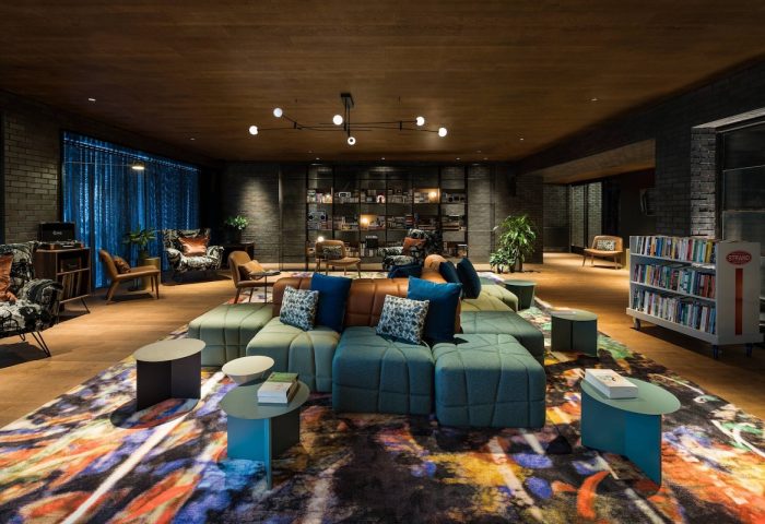 Moxy NYC East Village hotel's stylish lounge. Modern design, colorful rug, modular seating, and bookshelves create a welcoming, gay-friendly space.