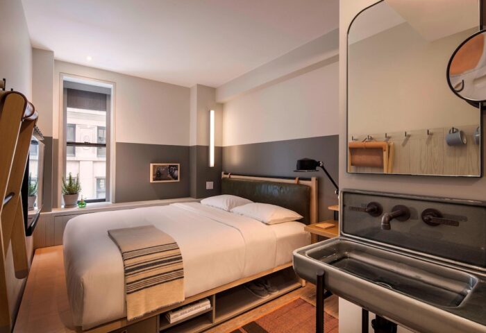 Moxy NYC Times Square hotel room. Gay-friendly hotel with bed, unique sink, and city view. Great for gay men travel in New York City.