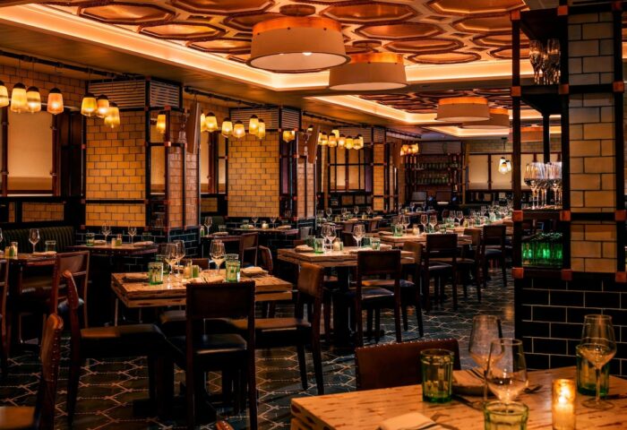 Moxy NYC Times Square gay-friendly hotel restaurant. Tables set, warm lighting, brick walls, and stylish decor. Upscale dining experience.