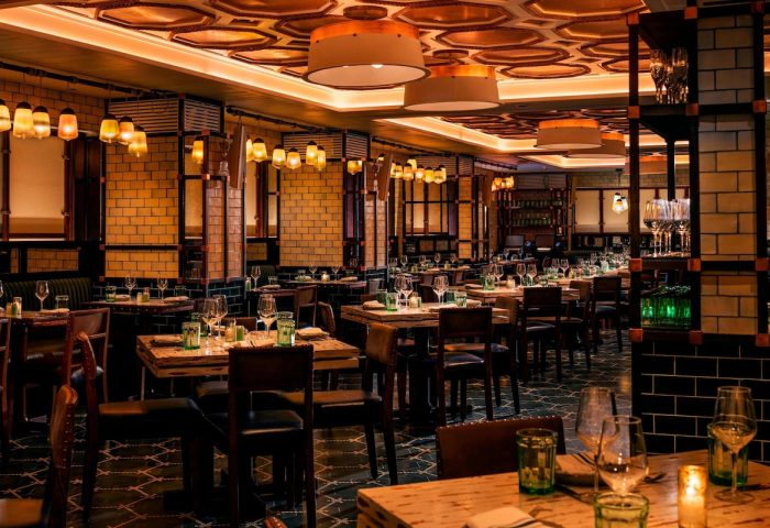 Moxy NYC Times Square gay-friendly hotel restaurant. Tables set, warm lighting, brick walls, and stylish decor. Upscale dining experience.