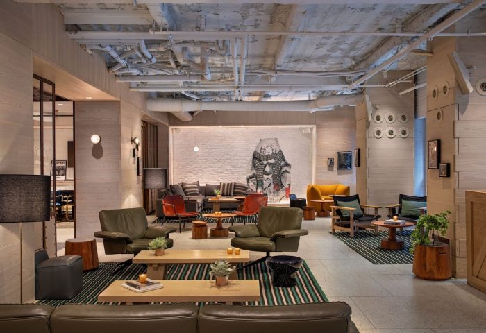 Moxy NYC Times Square gay-friendly hotel lobby. Lounge area with sofas, chairs, tables, and artwork. Modern, stylish interior design.