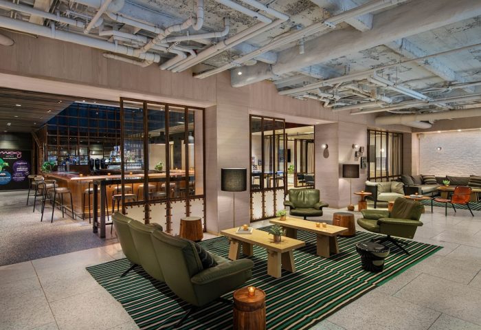 Moxy NYC Times Square gay-friendly hotel lounge area. Modern design with exposed pipes, bar, and comfortable seating for LGBTQ+ travelers.