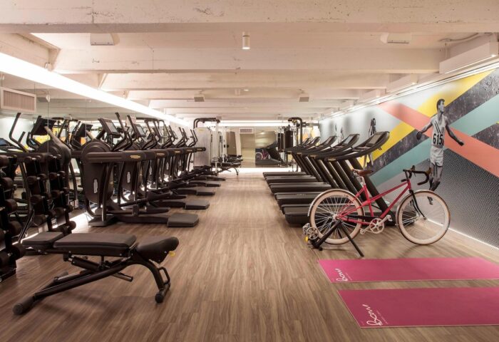 Moxy NYC Times Square gay-friendly hotel gym with treadmills, ellipticals, weights, yoga mats, and a pink bicycle. Fitness center.
