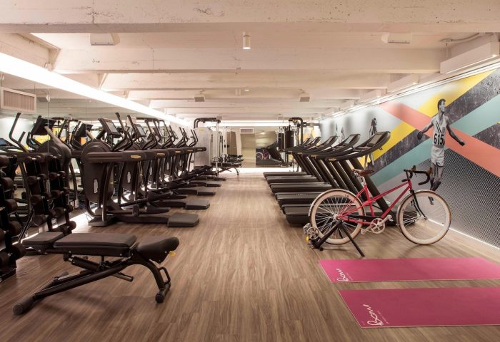 Moxy NYC Times Square gay-friendly hotel gym with treadmills, ellipticals, weights, yoga mats, and a pink bicycle. Fitness center.