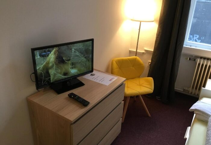 My Gayhostel detail: Gay-friendly hotel room interior. TV atop dresser, yellow chair, lamp. Comfortable stay for gay men travelers.