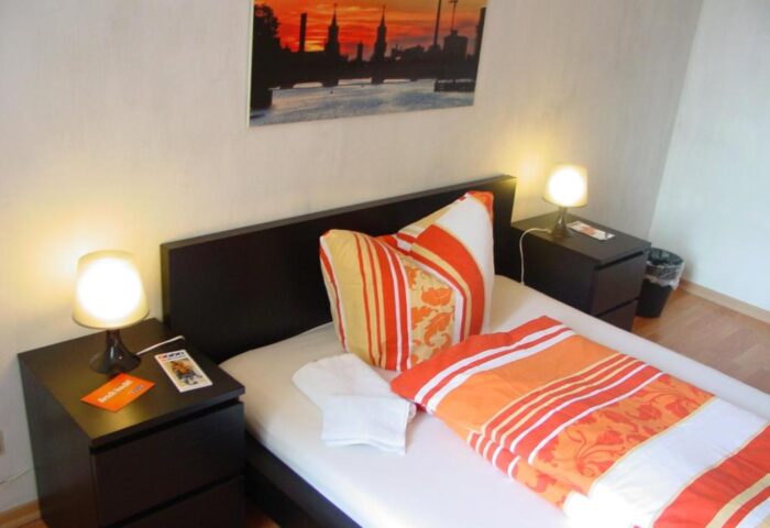 My Gayhostel room: Cozy gay-friendly hotel room with bed, nightstands, lamps, and Berlin skyline art. Ideal for gay men travel in a welcoming space.