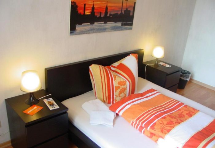 My Gayhostel room: Cozy gay-friendly hotel room with bed, nightstands, lamps, and Berlin skyline art. Ideal for gay men travel in a welcoming space.