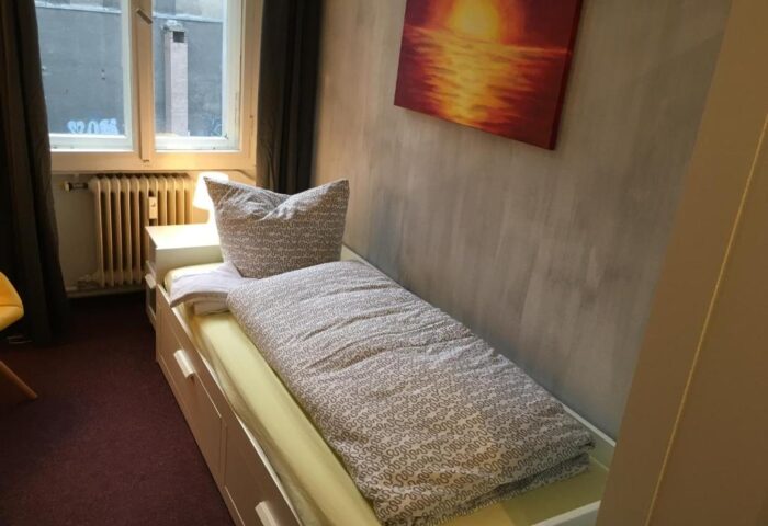 My Gayhostel room. Interior of a gay-friendly hotel, single bed, window, and sunset painting. Travel advice for gay men.